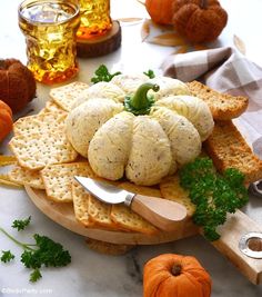 an assortment of cheese and crackers on a cutting board with pumpkins in the background