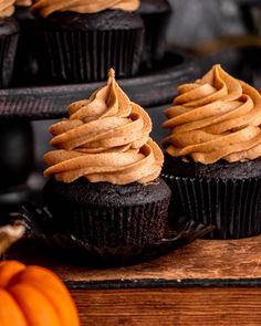 three cupcakes with frosting and pumpkins in the background