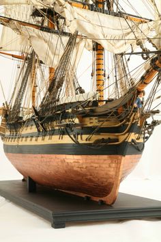 a wooden model ship with sails and masts on a black stand against a white background