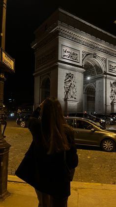 a woman is standing in front of the arc de trioe triumph at night time