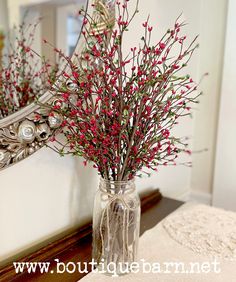 a vase filled with red berries sitting on top of a table next to a mirror