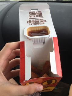 a person is holding up a box with some food in it that has ketchup on top