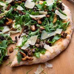 a pizza sitting on top of a wooden cutting board covered in greens and cheeses