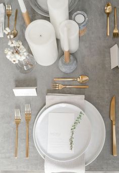 the table is set with gold and white plates, silverware, napkins, candles, and flowers