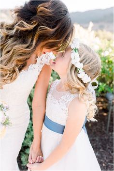 two brides are touching each other in front of some bushes and flowers on their wedding day