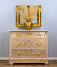 a gold and white dresser with a golden vase on top