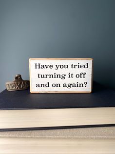 a wooden sign that says have you tried turning it off and on again? next to a book