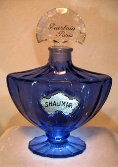 a blue glass bottle sitting on top of a white tableclothed surface with the label shalimar printed on it