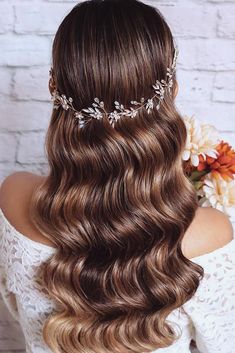 the back of a woman's head with long wavy hair and flowers in her hair