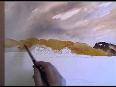 a person is holding a paintbrush in their hand while painting a landscape with watercolors