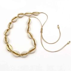 a gold necklace with white beads is shown on a white surface and has a cord attached to it