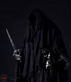 a man dressed in black with two large swords and skulls on his hands, standing against a dark background