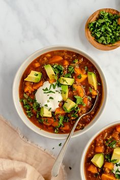 two bowls of chili with avocado, sour cream and cilantro on the side