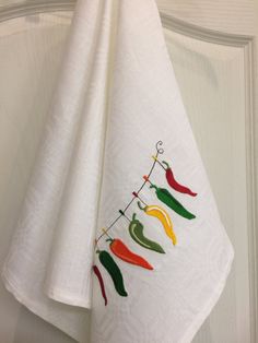 three white towels hanging from a hook with peppers on them