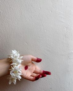 a woman's hand holding white flowers against a wall