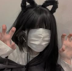 a woman with black hair wearing a white mask and bunny ears on her head, covering her face with both hands