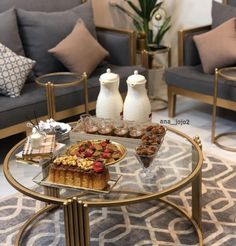 a glass table topped with desserts on top of a metal coffee table next to two couches