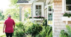 a man walking towards a house with flowers in the window boxes and plants growing outside