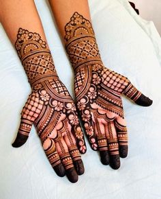 two hands with henna tattoos on them sitting on top of a white bed next to each other