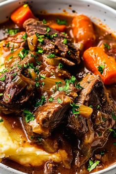 a white bowl filled with meat and potatoes covered in gravy, garnished with parsley