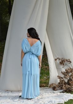 a woman in a blue dress standing next to a white structure with drapes on it