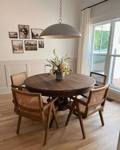 a wooden table with chairs around it in front of a large window and pictures on the wall