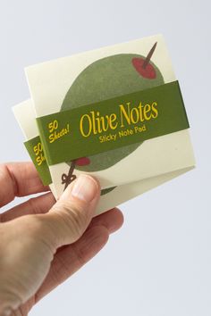 a person holding up an olde notes sticky note pad with apple on the front