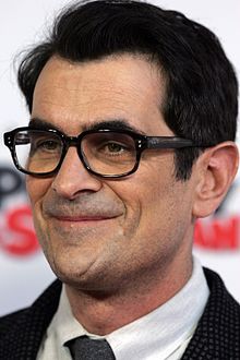 a close up of a person wearing glasses with a suit and tie in front of a white background