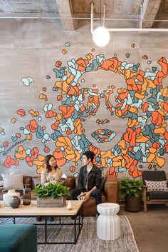 two people sitting on couches in front of a wall with flowers painted on it