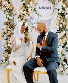 a man and woman sitting next to each other in front of a flower covered arch