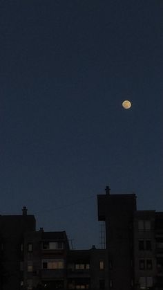 the moon is shining brightly in the sky above some apartment buildings at night with no clouds