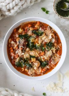 a white bowl filled with soup next to a spoon and some bread on the side