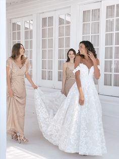 three women in dresses are standing near each other and one woman is holding her dress