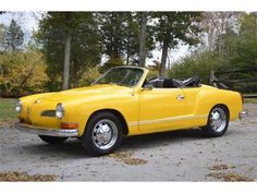 an old yellow convertible car parked in a parking lot next to a fence and trees