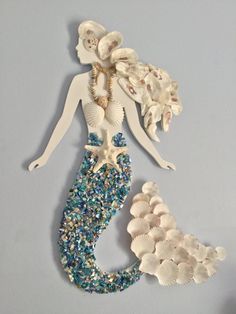 a white and blue mermaid with shells on it's back is standing in front of a gray wall