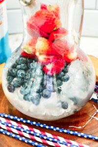 some strawberries and blueberries are in a glass vase on a wooden board with other items around it