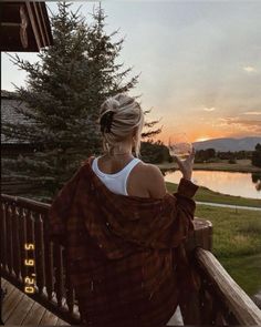 a woman sitting on a porch with a wine glass in her hand and the sun setting behind her