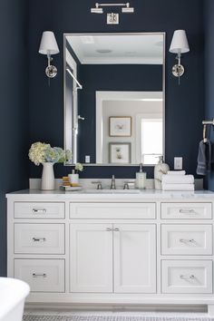 a bathroom with blue walls and white cabinetry has a large mirror over the sink