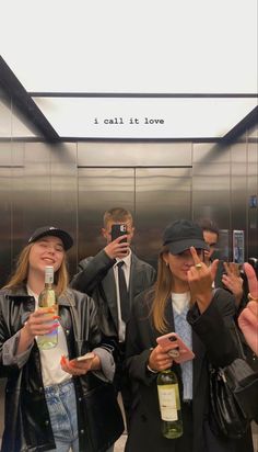 three people standing in an elevator taking pictures with their cell phones and holding wine bottles