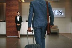 a man in a suit and tie pulling a suitcase with his hand on the handle