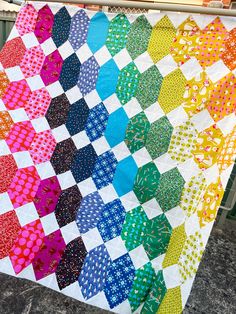 a multicolored quilt hanging on a clothes line with an umbrella in the background