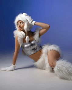 a woman in a silver outfit and furry white hat posing for the camera with her hands on her head