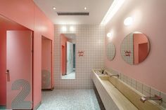 a bathroom with pink walls and two sinks in the middle, mirrors on the wall