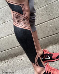 a man's legs with tattoos and running shoes on the ground next to a brick wall