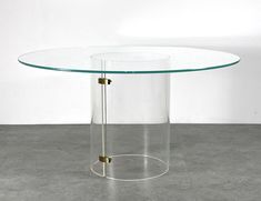 a round glass table with metal legs on concrete flooring and white wall in the background