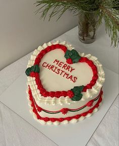 a heart - shaped cake with merry christmas written on it and holly leaves in the middle