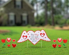 two hearts with wings are on the grass in front of a house and there is a sign that says happy valentine's day