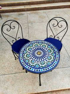 two wrought iron chairs and a table on the ground in front of some steps,