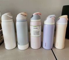 four different colored bottles lined up next to each other on a counter top in front of a wall