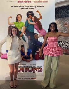 two women standing in front of a poster for the movie bottoms, which is on display